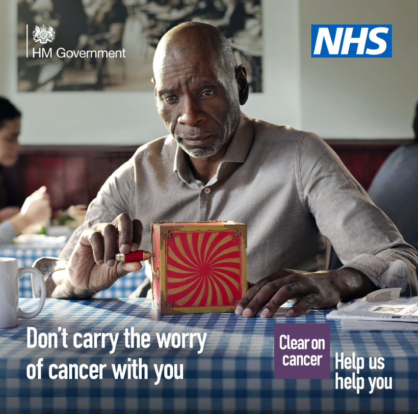 A middle-aged person sitting a cafe with a red jack-in-the-box toy on the table across from them. The person is looking at the red-jack-in-the-box with a concerned expression on their face. The text reads: Don’t carry the worry of cancer with you. The NHS logo is in the top right hand corner. A middle-aged person sitting a cafe with a red jack-in-the-box toy on the table across from them. The person is looking at the red-jack-in-the-box with a concerned expression on their face. The text reads: Don’t carry the worry of cancer with you. The NHS logo is in the top right hand corner.